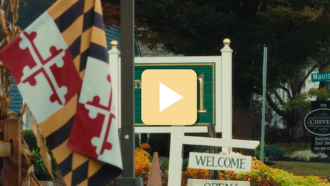 Decorative flags with a play button overlay in front of a 'Welcome' sign.