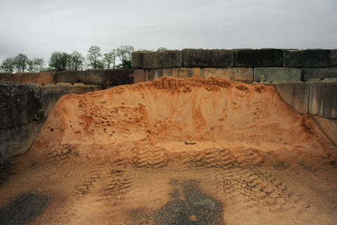 Large stone basin with a textured surface, surrounded by a stone wall on a cloudy day.