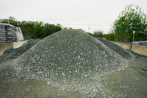 Large pile of gravel or crushed stone with trees and a clear sky in the background
