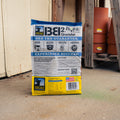 A bag of Big & J® BB2 Enhance Corn Pellet Attractant deer attractant stands on a concrete floor in front of a weathered wooden door, with stacked terracotta pots visible in the background.
