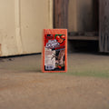 A package of Buck Lickers wild persimmon salt block standing upright on a concrete floor in an outdoor or semi-outdoor setting with a blurred background.