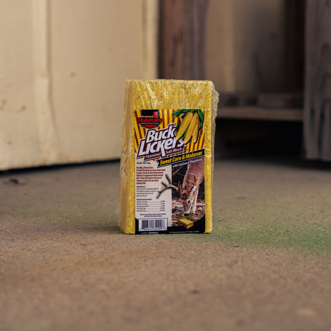 A packaged yellow salt block with a Buck Licker label, standing upright on a concrete floor in an indoor setting.
