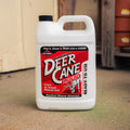 A white plastic jug of Deer Cane Lick, set on a concrete floor in front of a rustic wooden wall.