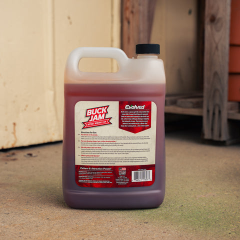 A large plastic jug of Buck Jam mineral lick standing on a concrete floor in front of a rustic wooden door.