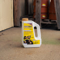 A white plastic jug of MoleMax Mole and Vole Repellent ground bait with a yellow label and tan cap, standing on a concrete floor in an outdoor storage area.