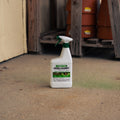 A white spray bottle of Deer & Rabbit Repellent standing on a concrete floor in a workshop or shed, with wooden pallets and terracotta pots in the background.
