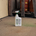 A white spray bottle of deer and rabbit repellent with a green trigger sprayer, standing on a concrete floor in a workshop or garage setting.