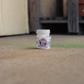 A small white plastic jar of Mole Stopper Smoke product standing on a textured concrete floor in an outdoor or industrial setting.