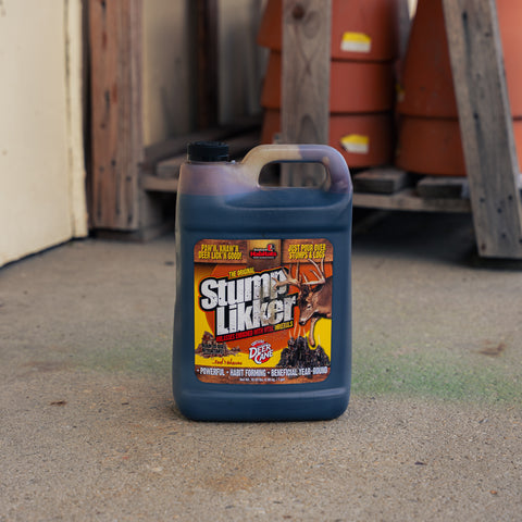 A large plastic jug of Stump Likker stands on a concrete floor in front of a wooden shed with stacked terracotta pots in the background.