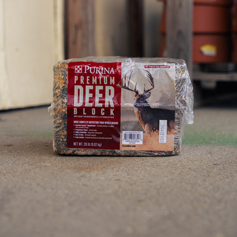 A package of Purina Premium Deer Block bedding, wrapped in clear plastic, standing on a concrete floor in an outdoor or workshop setting.