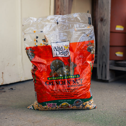 A bag of Wild Life Design Crunchin' Nut birdseed on a concrete floor in front of a white wall and wooden structure.