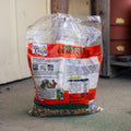 A bag of Wild Life Design Crunchin' Nut birdseed on a concrete floor in front of a white wall and wooden structure.