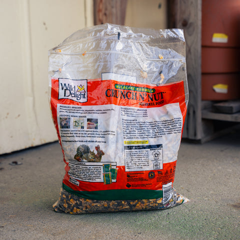 A bag of Wild Life Design Crunchin' Nut birdseed on a concrete floor in front of a white wall and wooden structure.