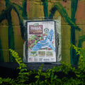 A package of Dalen BirdX Protective Netting For Fruit, shown in its clear plastic packaging with a printed label featuring a blue bird and product details, set against a painted brick wall with green foliage in the foreground.
