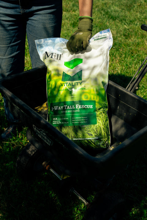 Person holding a bag of 'Vitality' fertilizer in a garden cart.