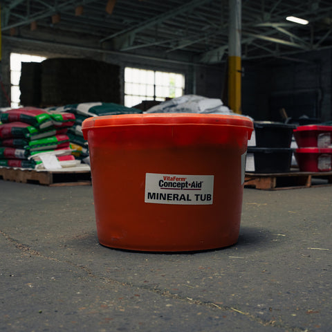 An orange-red plastic mineral tub with a white label reading 'VitaFerm Concept-Aid MINERAL TUB' in a warehouse setting.