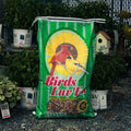 A large green bag of Birds Luv' Em Classic Blend featuring a red cardinal and a small bird on a yellow sunflower graphic, set on gravel in a garden center with potted plants in the background.