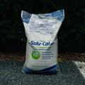 A large white bag of Solu-Cal USA Enhanced Calcium Products standing on asphalt outdoors with dark green foliage in the background.