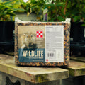 A 20 lb block of Purina Premium Wildlife Block supplement, displayed on a wooden table in a greenhouse setting with other plants in the background.