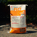 A large bag of Purina Impact Hay Stretcher Pelleted horse feed standing upright outdoors on gravel with dark foliage in the background.