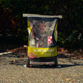 A bag of Purina Supersport horse supplement standing upright on an outdoor paved surface with trees and shrubs in the background.