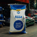 A large bag of Kent Blue Seal Animal Feed standing on a warehouse floor, with other bags of feed stacked in the background.