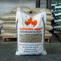 A large white bag of Supreme Heat Hardwood Blend Fuel Pellets standing on a pallet in a warehouse setting, with other bags stacked in the background.