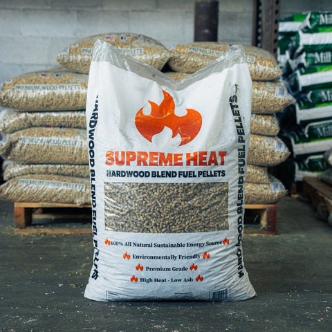 A large white bag of Supreme Heat Hardwood Blend Fuel Pellets standing on a pallet in a warehouse setting, with other bags stacked in the background.