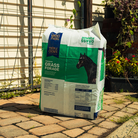 A bag of Triple Crown Premium Grass Forage sitting on a patio with plants in the background