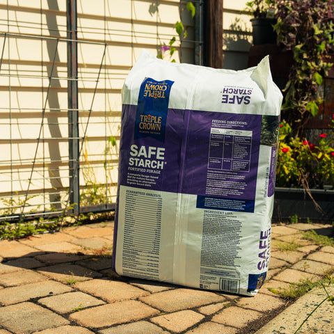 A bag of Triple Crown Safe Starch Forage sitting on a patio with plants in the background
