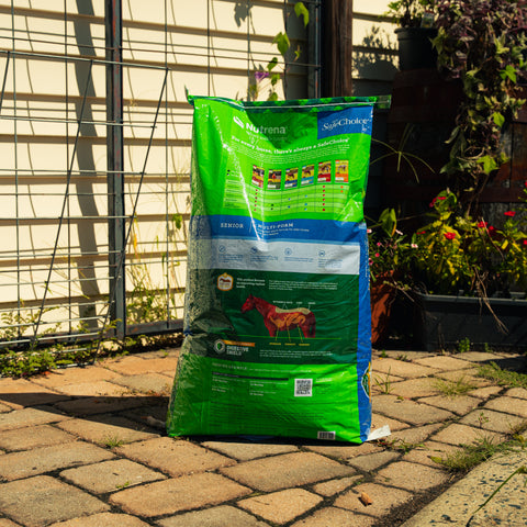 Nutrena SafeChoice Senior Horse Feed bag with labeled nutrition info and a horse grazing nearby, designed for senior horses.