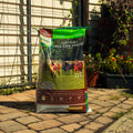 A large bag of Natural Balance Safe-Choice All Life Stages Premium Horse Feed stands on a stone patio in a backyard setting with a fence and plants in the background.