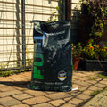 A large black bag of ProForce Fuel supplement stands on a paved patio in front of a garden fence and trellis, with plants visible in the background.