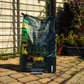 A large black bag of ProForce Fuel XF supplement stands on a paved patio in front of a garden fence and trellis, with plants visible in the background.