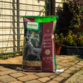 A large bag of Empower Boost supplement stands on a paved patio in front of a garden fence and trellis, with plants visible in the background.