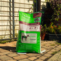 A large bag of Empower Boost supplement stands on a paved patio in front of a garden fence and trellis, with plants visible in the background.