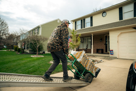 Person pushing a cart with bags on a driveway in front of a house