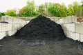 Heap of compost against a concrete wall with trees in the background