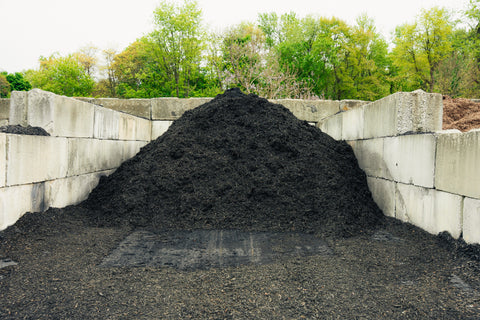 Heap of compost against a concrete wall with trees in the background