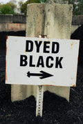 Sign with 'DYED BLACK' text and an arrow pointing right, attached to a concrete block.