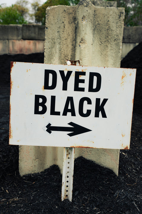 Sign with 'DYED BLACK' text and an arrow pointing right, attached to a concrete block.