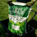 Bag of turf fertilizer held by a person with gloves on a grassy background