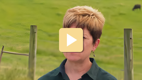 woman standing near fence with play button overlay
