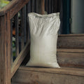 A large off-white woven sack with black printed text stands on rustic wooden steps next to a wooden railing.