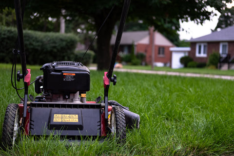 image of a push lawn mower sitting on grass with houses in the distance