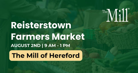 Promotional graphic for the Reisterstown Farmers Market at The Mill of Hereford, featuring white text over a dark green, slightly blurred background showing produce baskets and a person's hands.