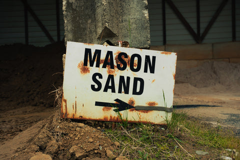 Rust-covered sign pointing to 'Mason Sand' with a arrow on a dirt ground.
