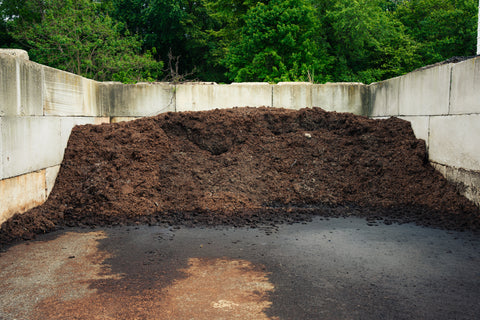 Heap of compost in a concrete area with greenery in the background