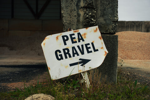 Rust-covered sign pointing to 'Pea Gravel' on a grassy area.