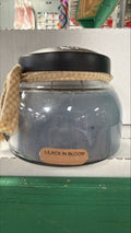 A Cheerful Giver Lilacs in Bloom candle with a white ceramic container showcasing a floral lilac design and soft candle wax inside.